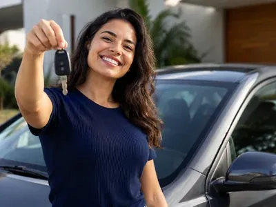 Mulher de cabelo escuro levantando a chave de um carro cinza no momento da entrega do veículo
