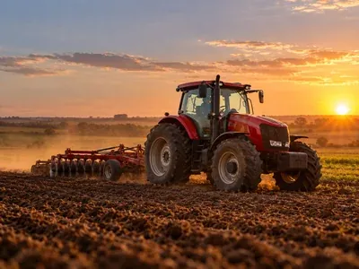Trator vermelho arando a terra em uma lavoura ao pôr do sol
